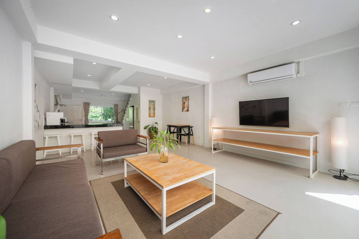 Een moderne woonkamer met een bank, salontafel, televisie en een keuken op de achtergrond.