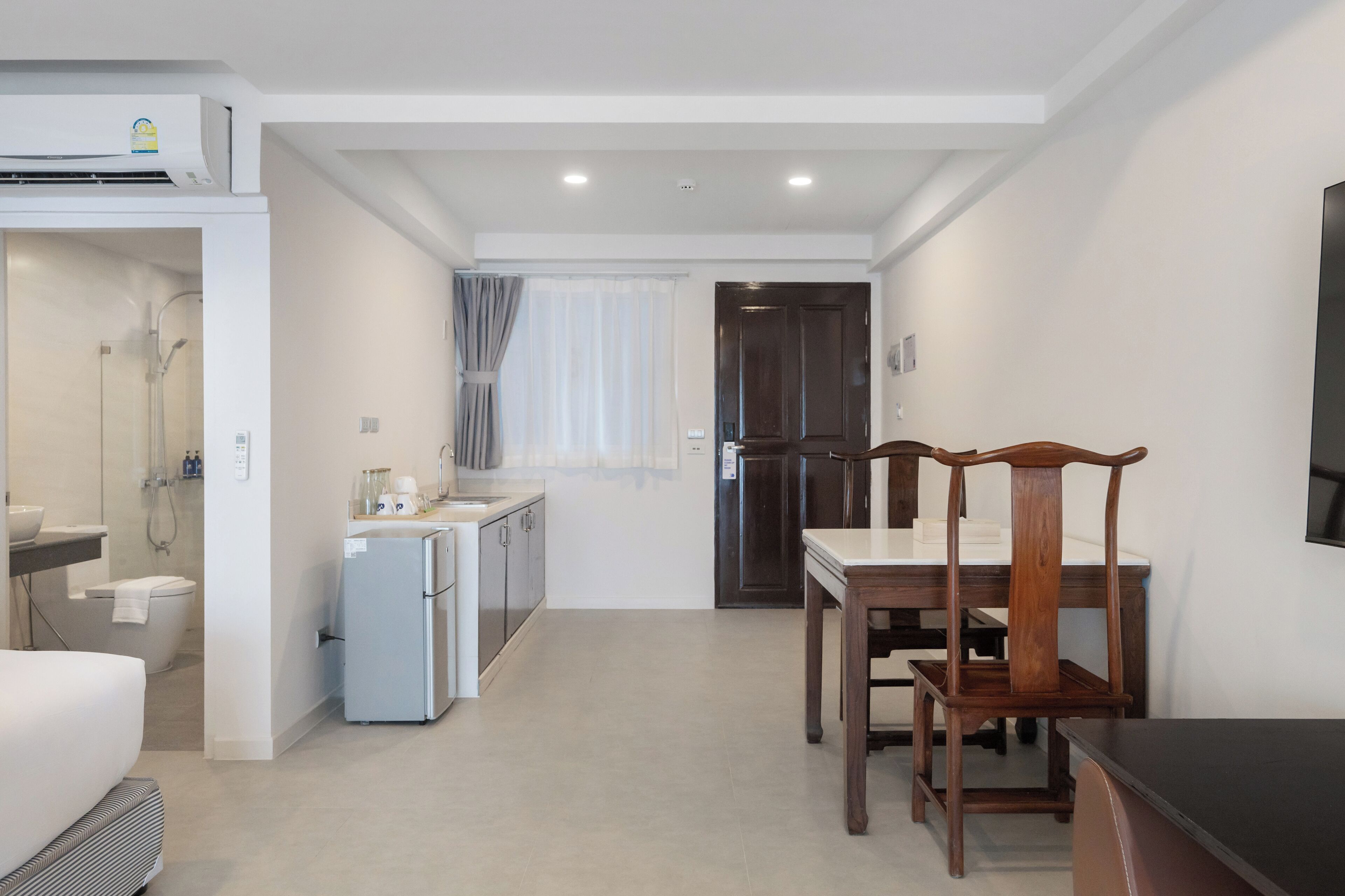 Een compacte hotelkamer met een kitchenette, een zithoek met een houten tafel en stoelen, een douche en een donker houten deur.