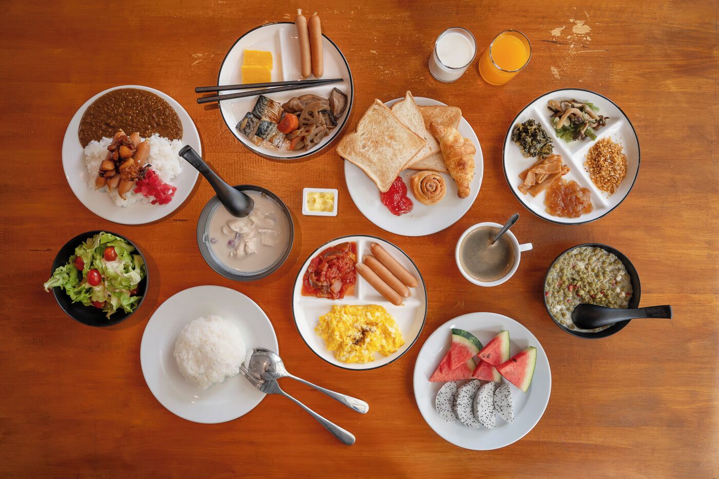 Una mesa con diversos platos, como arroz, sopa, huevos, salchichas y fruta.