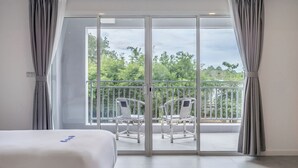 Habitación de hotel con un amplio ventanal corredero que da a un balcón con dos sillas.