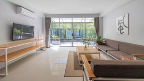 Una sala moderna con una televisión de pantalla plana, muebles de madera, un sofá y un ventanal con vistas a la vegetación.