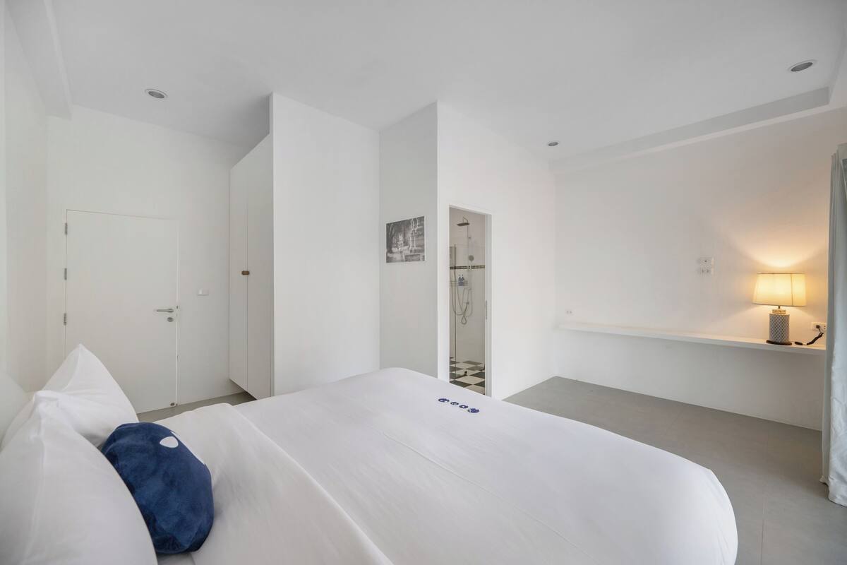 Een hotelkamer met een bed, een nachtkastje met lamp, een deur en een douchehoek.