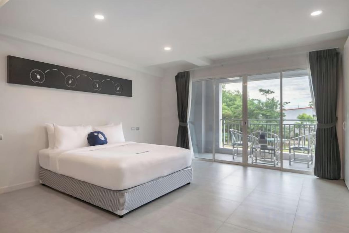 Habitación de hotel moderna con una cama grande, un balcón con sillas y vistas al exterior.