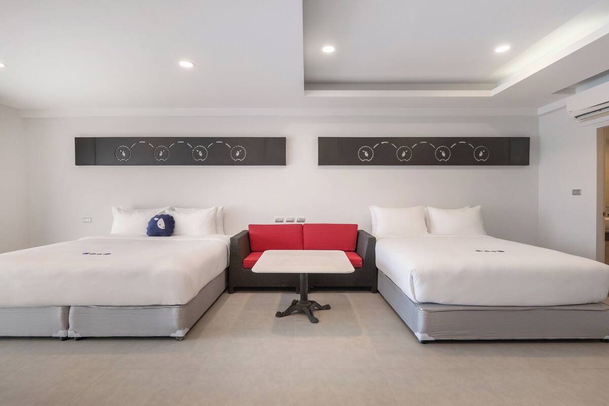 Een moderne hotelkamer met twee bedden, een rode bank in het midden en een kleine tafel.