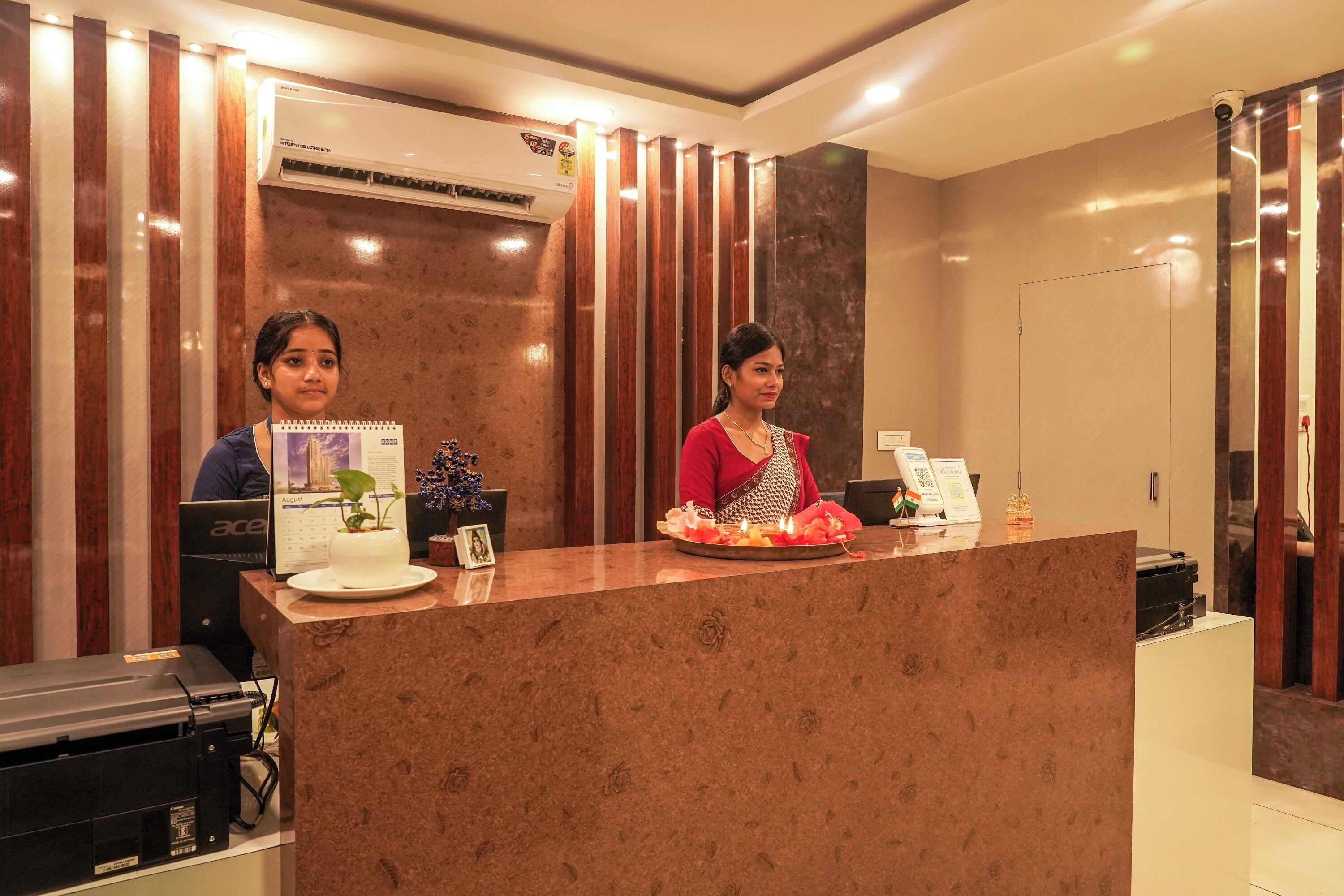 A reception desk with two staff members, a calendar, a small plant, and a tray with food items.