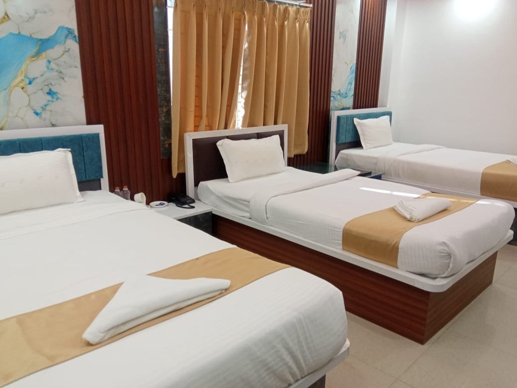 A hotel room with three single beds, a wooden headboard, a large window with curtains, and a marble wall art piece.