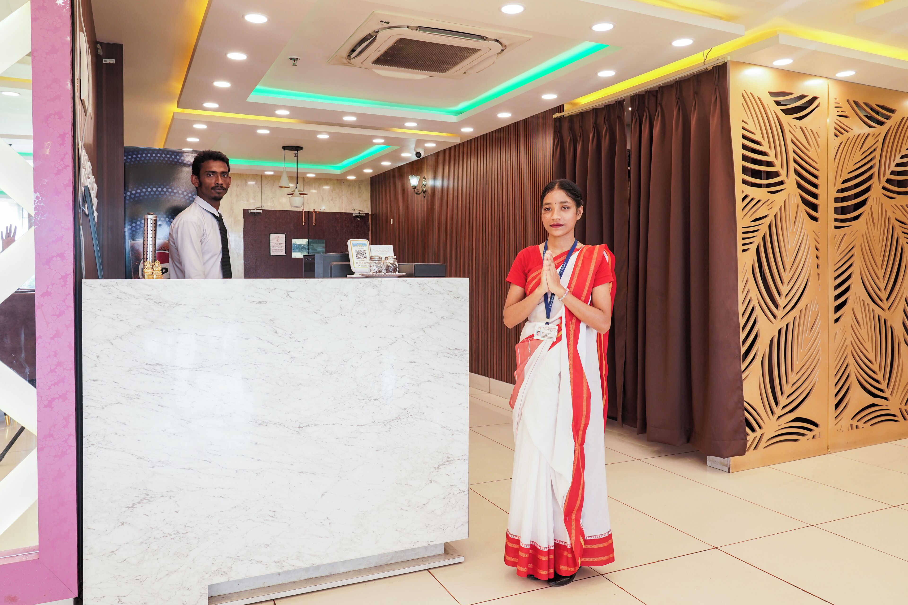 A hotel reception area with a marble counter, wooden paneling, and a modern ceiling design.