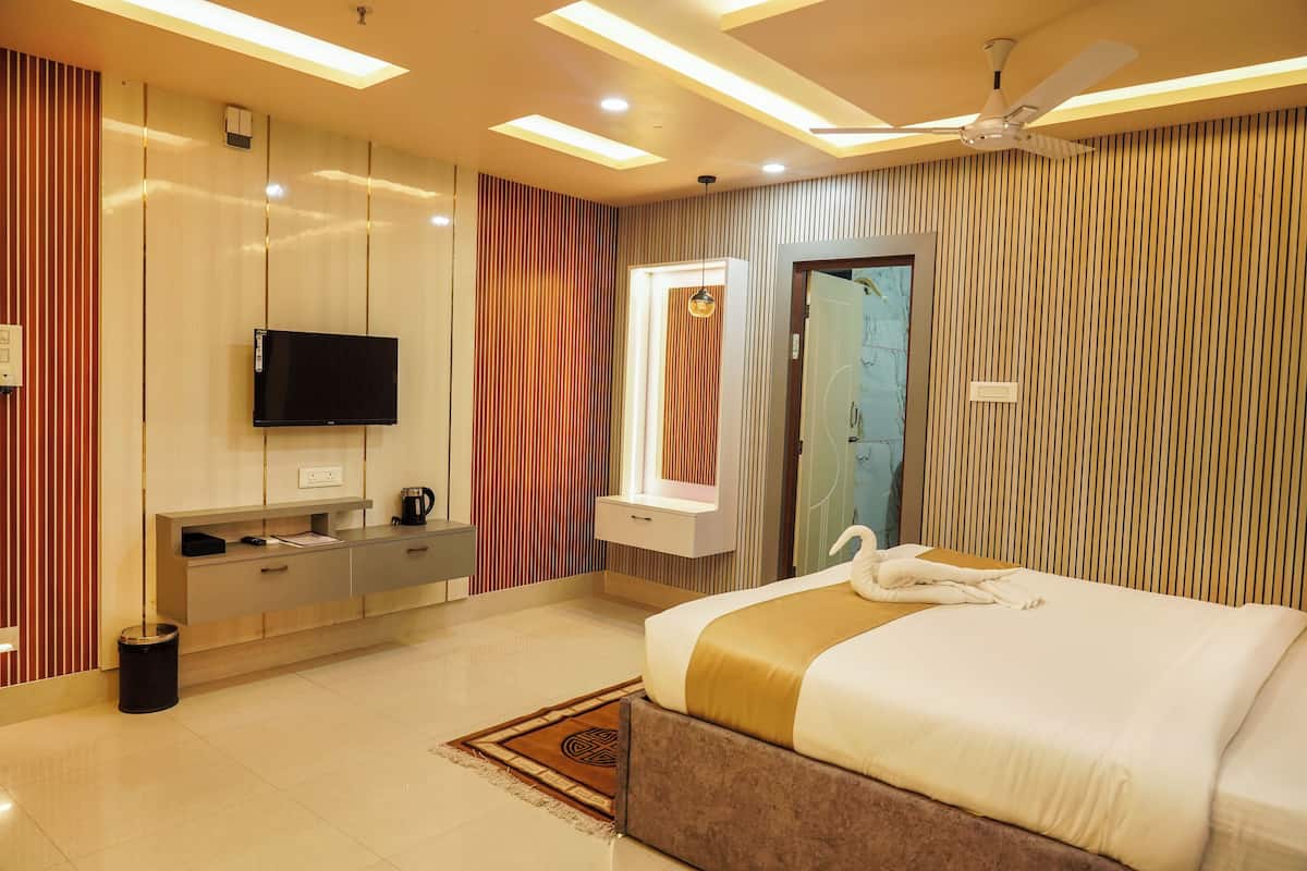 A modern hotel room with a large bed, a flat-screen TV, a vanity with a mirror, and a ceiling fan.