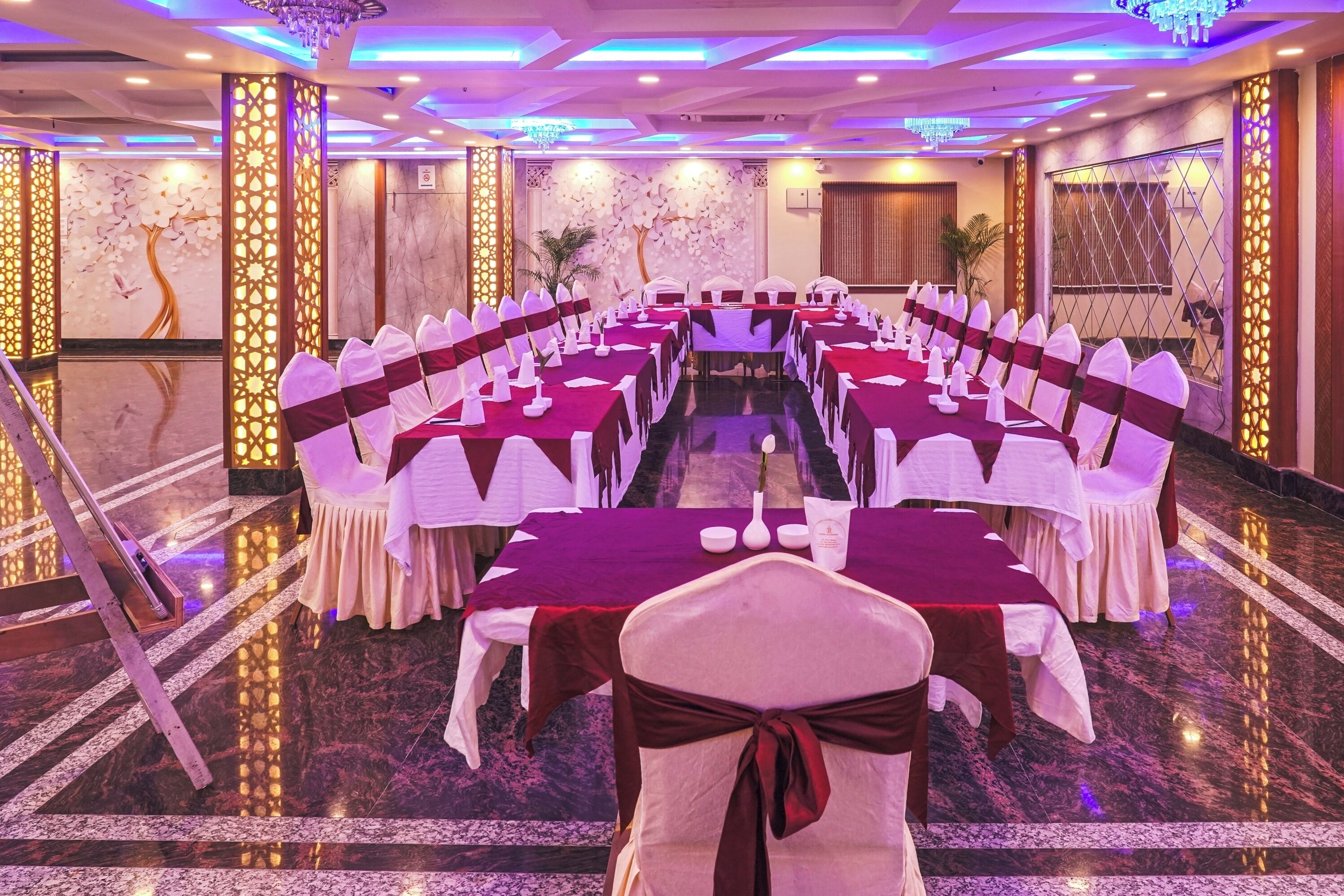 Un salón de banquetes con filas de mesas y sillas, una araña y paneles decorativos en las paredes.