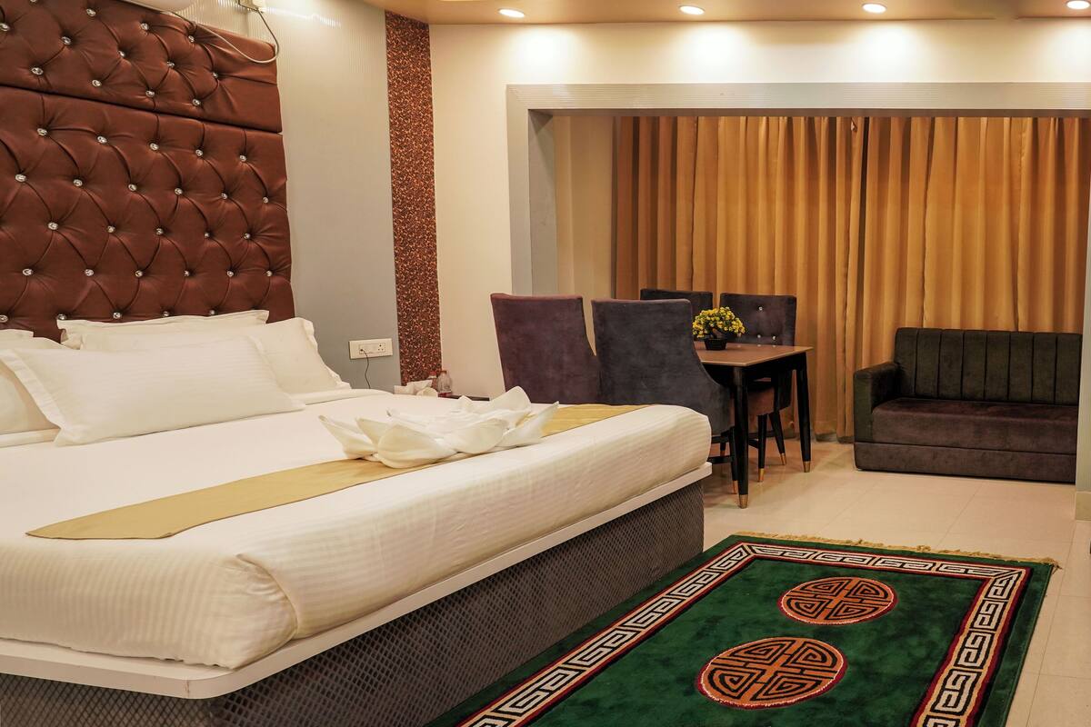 A hotel room with a large bed, a desk with a chair, a television, and a view of the outside through curtains.