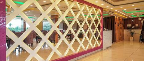 A modern hotel lobby with a geometric decorative wall, a reception desk, and a clean, tiled floor.