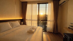 Habitación de hotel con una cama grande, una ventana con cortinas y vistas al atardecer, además de un aire acondicionado.
