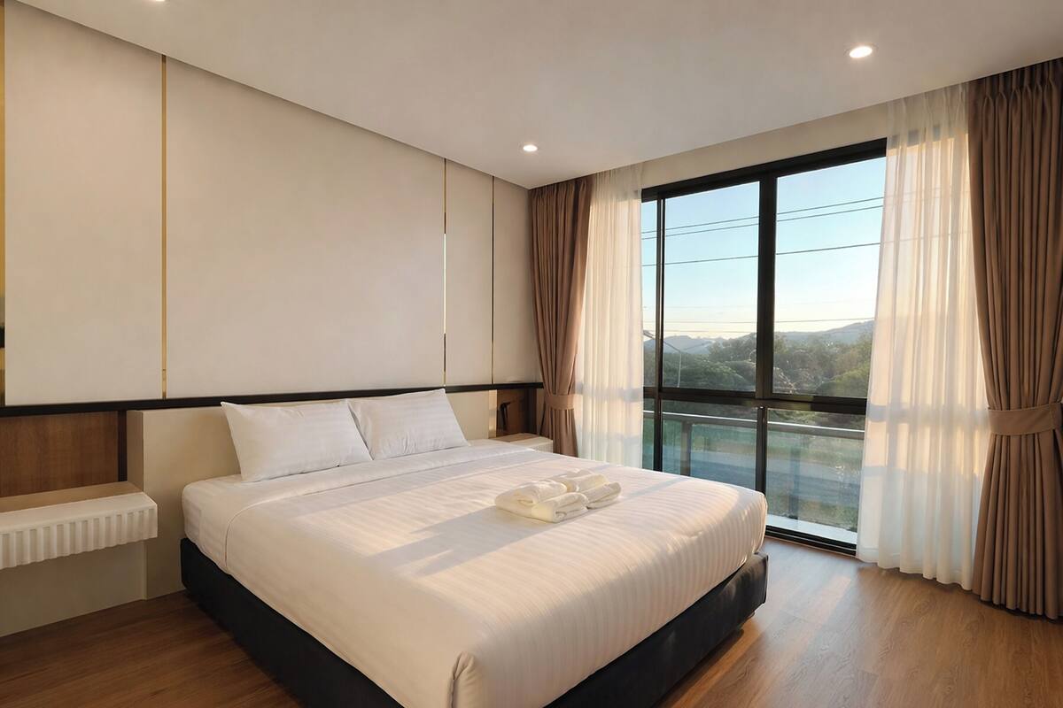 A modern hotel room with a large bed, a view of the outdoors, and a window with curtains.