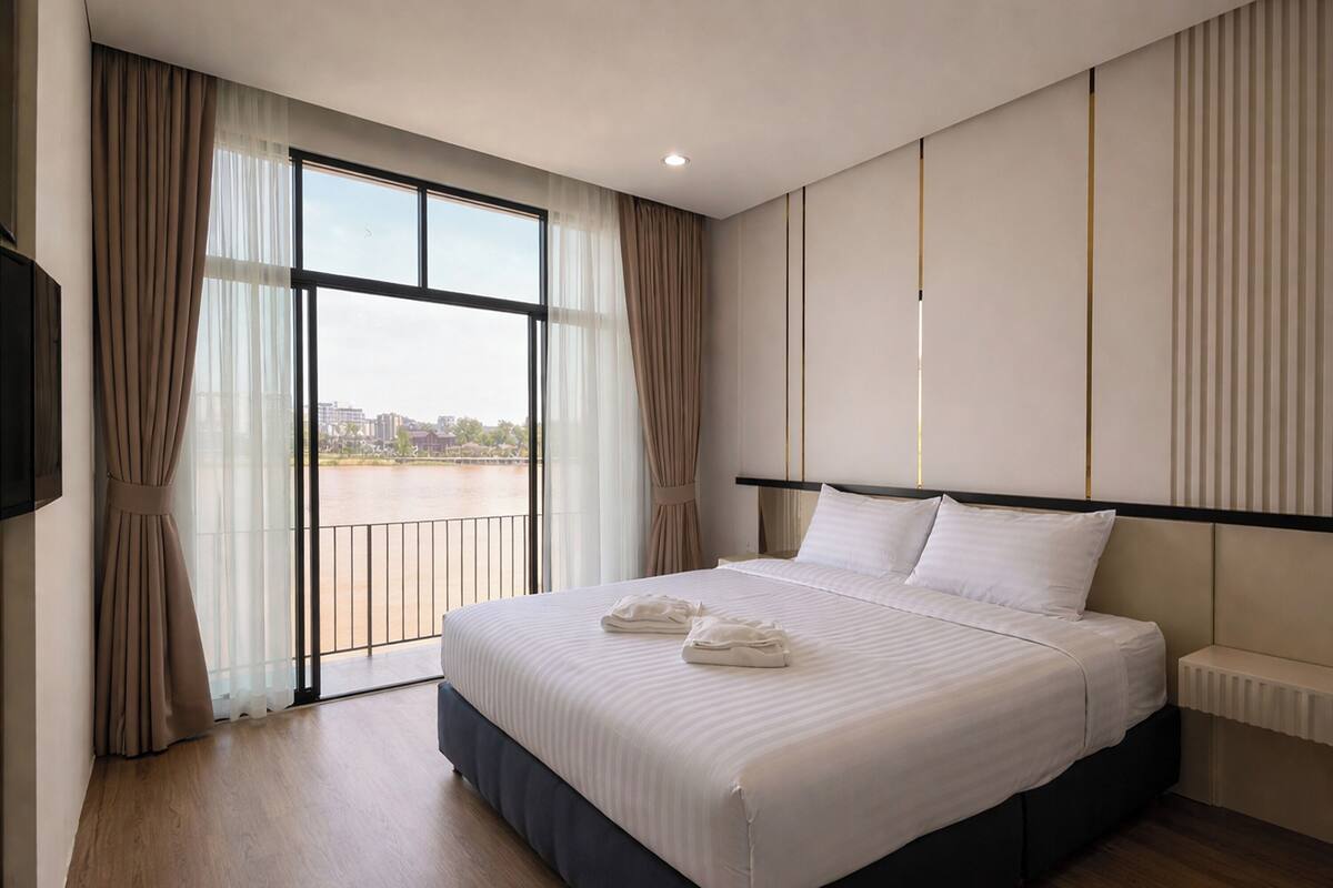 A hotel room with a large bed, a view of a river, and a modern design.