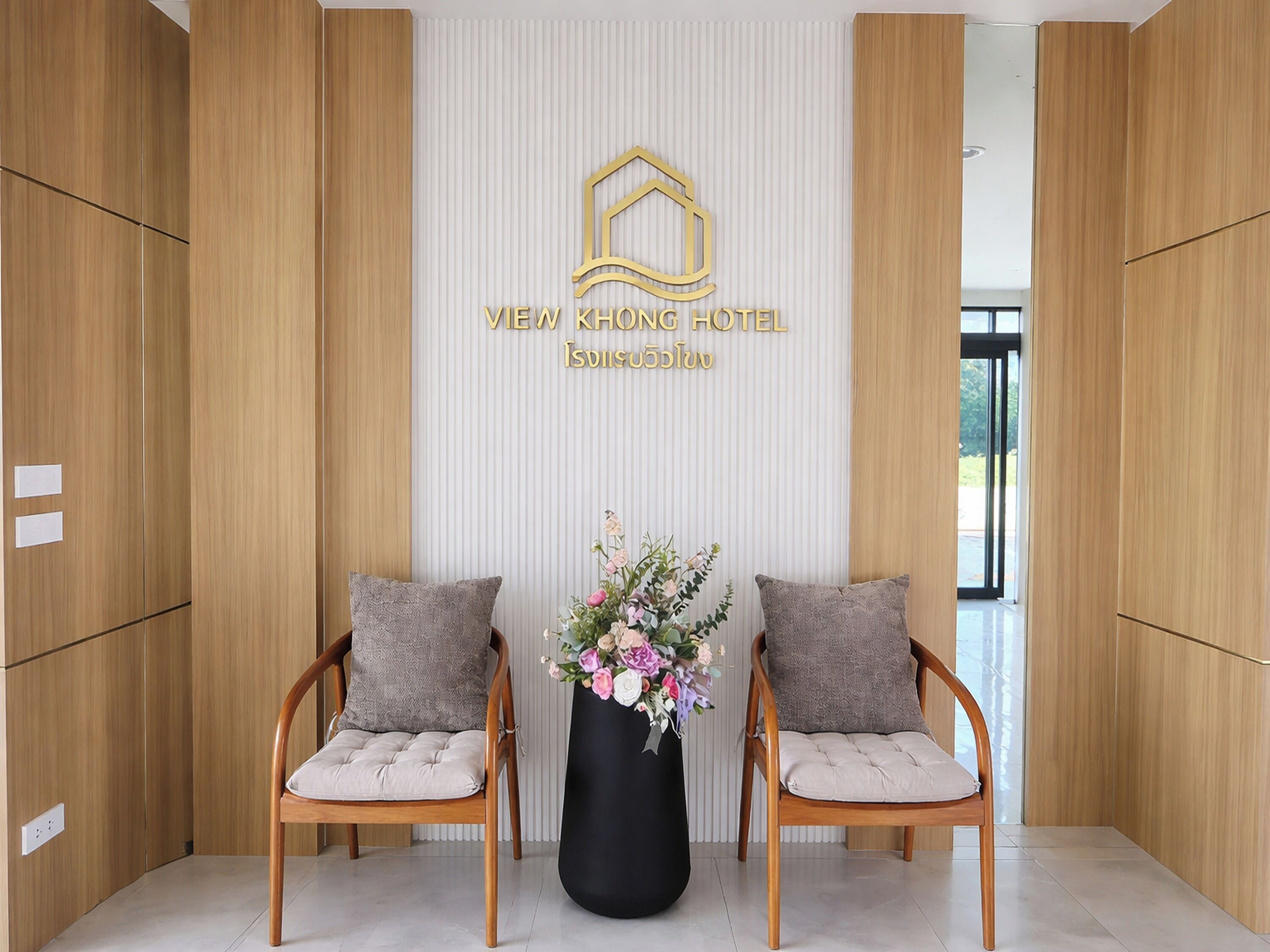 En reception med en træreception, to polstrede stole, en sort vase med blomster og et vægmonteret skilt med hotellets navn.