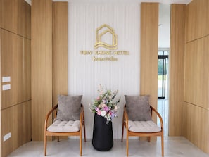 A reception area with a wooden reception desk, two cushioned chairs, a black vase with flowers, and a wall-mounted sign with hotel name. - View khong Hotel (Chiang Saen)