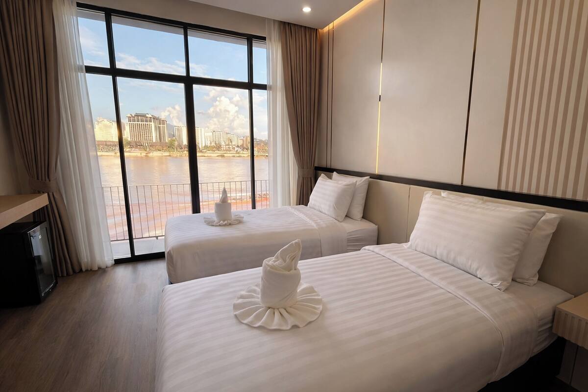 A hotel room with two beds, a TV, and a view of a cityscape and water.