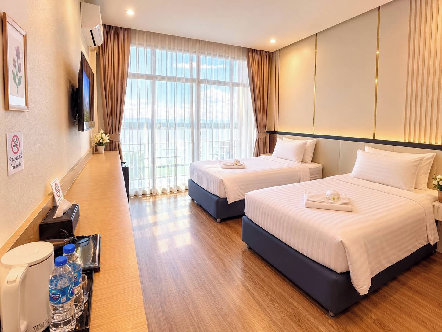 A hotel room with two beds, a desk with a water dispenser, and a large window with curtains.
