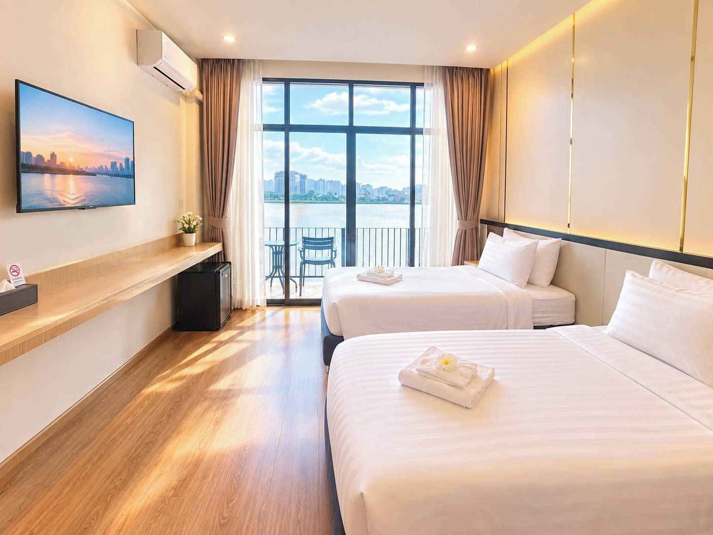 Ett hotellrum med två sängar, ett skrivbord, en TV och en balkong med utsikt över staden.