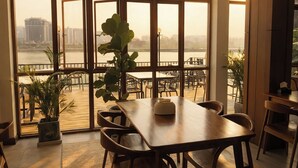 Un comedor con un amplio ventanal que da a un río, muebles de madera y plantas en macetas.
