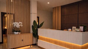 Un mostrador de recepción con paneles de madera, una planta en maceta y un letrero que indica TPBOX.