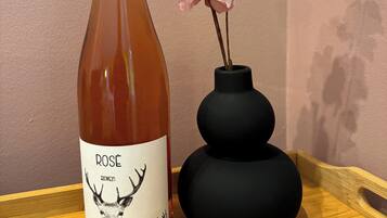 Eine Flasche Roséwein mit Hirsch-Illustration und dem Text "Rose" und "Bovine Wild" auf dem Etikett, platziert auf einer Holzschale neben einer schwarzen Vase mit rosa Blumen.