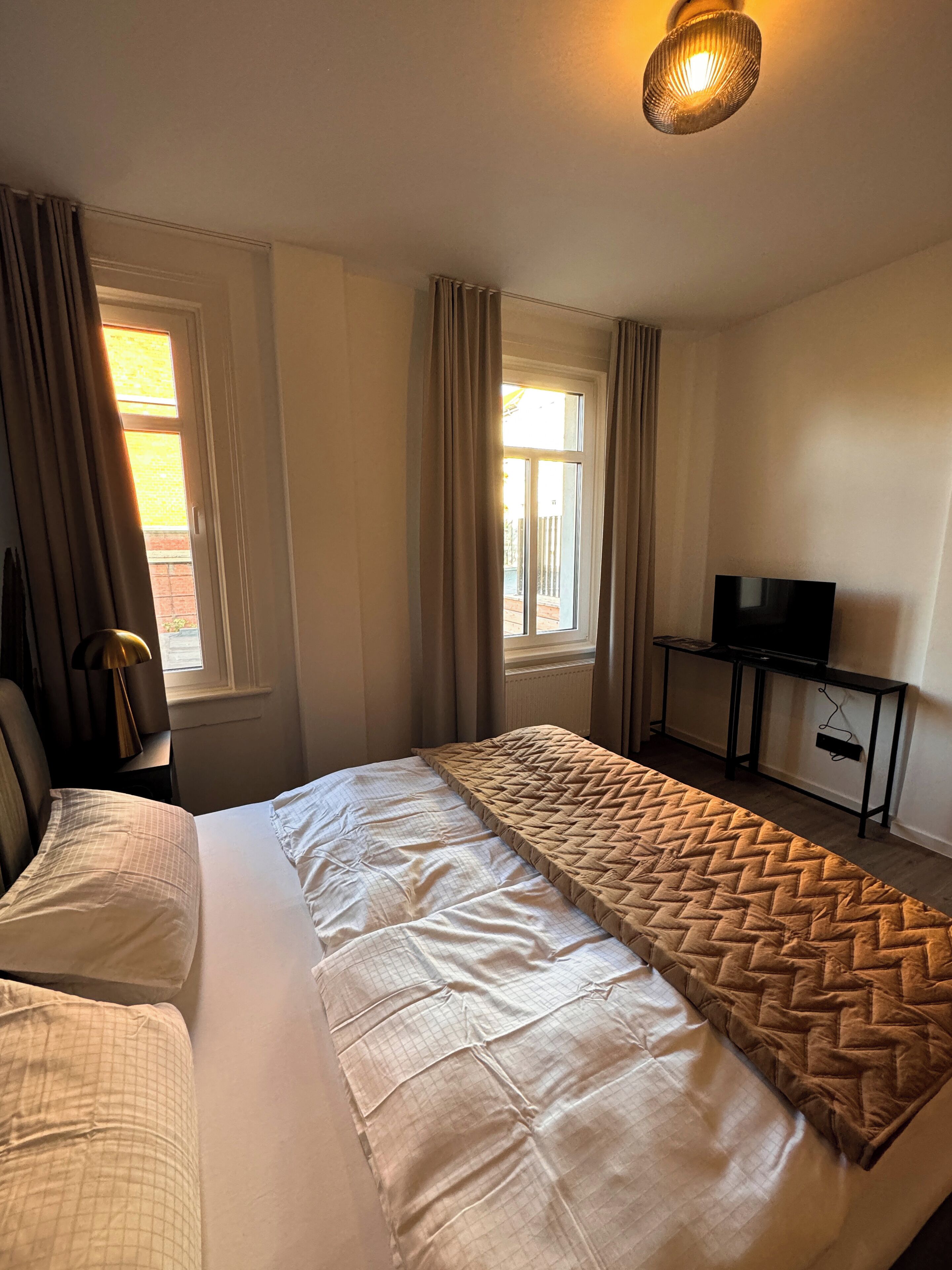 Ein Hotelzimmer mit Bett, Fernseher auf einem Schrank und einem Fenster mit Vorhängen.