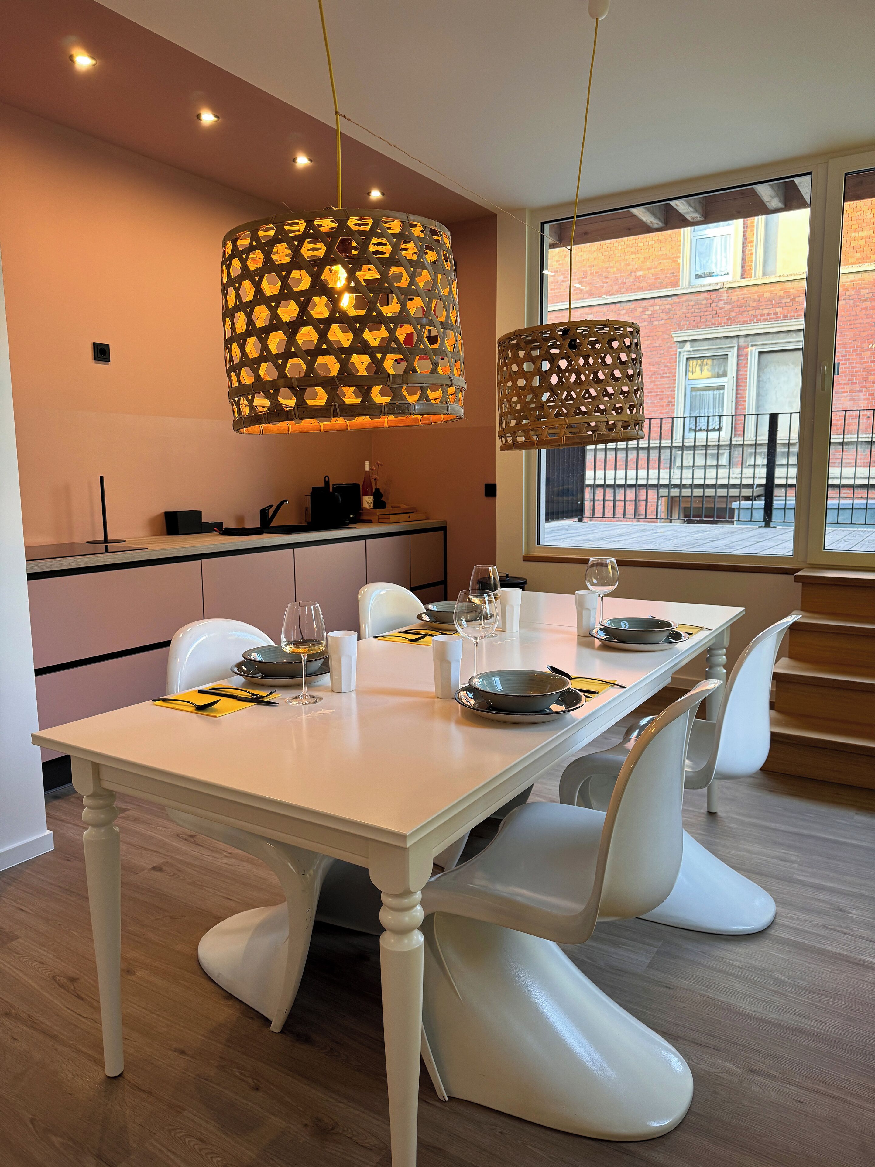 A modern dining area with a white table set for four, white chairs, and two hanging pendant lights.