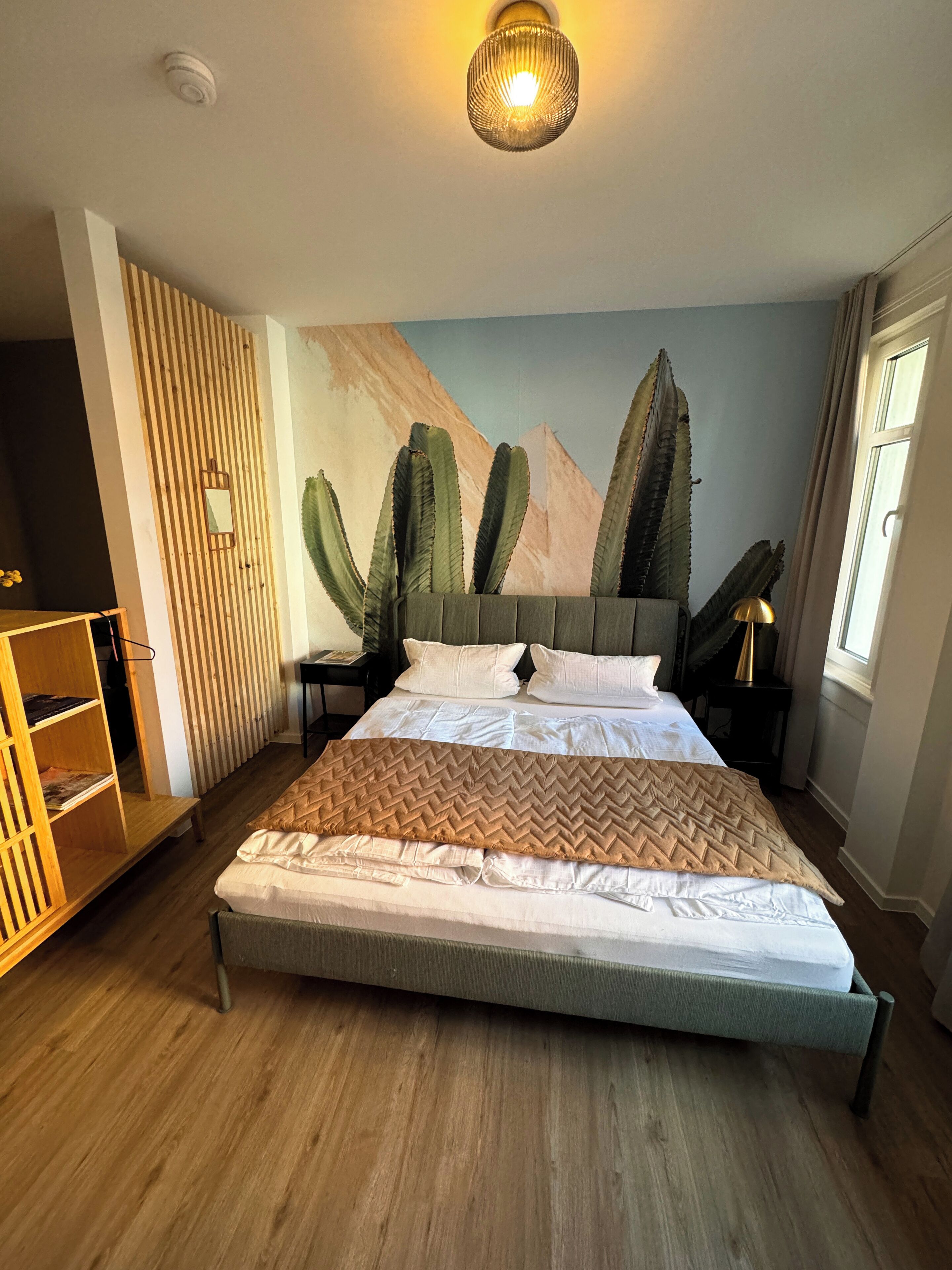 Une chambre à coucher avec un lit, un plancher en bois, une fresque murale représentant des cactus et un luminaire au plafond.