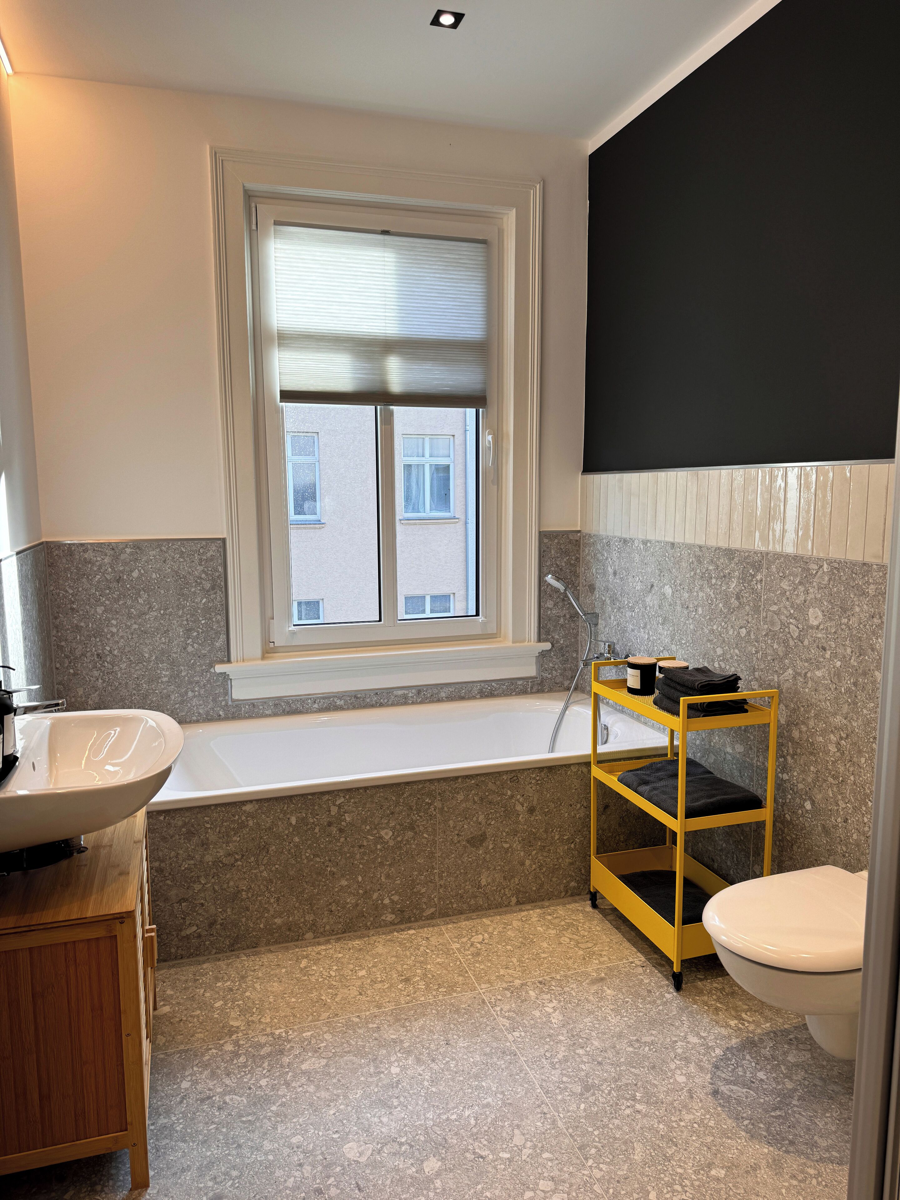 Een badkamer met een bad, een wastafel, een toilet en een raam met zonwering.