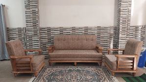 Un salon comprenant un ensemble de canapés, deux fauteuils en bois et un tapis à motifs.