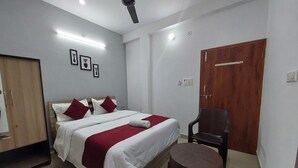 Une chambre d’hôtel avec un lit, une armoire en bois, une chaise et un petit tabouret.