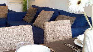 Una sala de estar moderna con un sofá azul, cojines color beige y una mesa de comedor con un jarrón blanco y un cuenco.