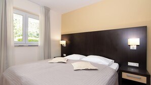 Habitación de hotel con una cama grande, dos mesitas de noche, una ventana con cortinas y luces fijadas a la pared.