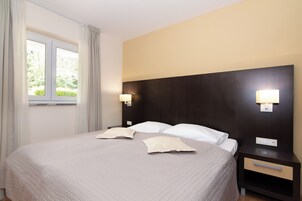 Habitación de hotel con una cama grande, dos mesitas de noche, una ventana con cortinas y luces fijadas a la pared.