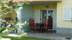 Un patio exterior con una mesa y cuatro sillas, una puerta de cristal y una pared amarilla.