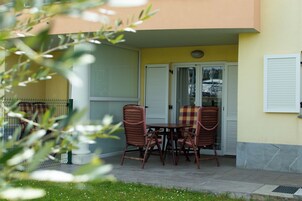 Un patio exterior con una mesa y cuatro sillas, una puerta de cristal y una pared amarilla.