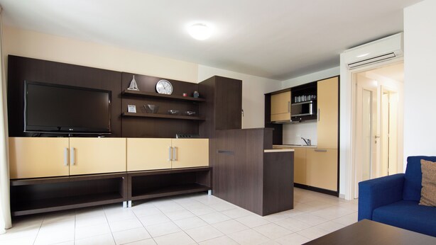 Una cocina moderna con electrodomésticos integrados, un televisor de pantalla plana y una zona de comedor con un sofá azul.