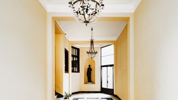 A grand hallway with a marble floor, a large chandelier, and a statue in the center.