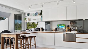 Una cocina moderna con armarios blancos, una mesa de comedor de madera y un amplio ventanal con vistas a zonas verdes.