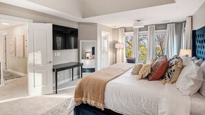 Un dormitorio espacioso con una cama grande, un televisor montado en la pared y vistas al exterior a través de la ventana.
