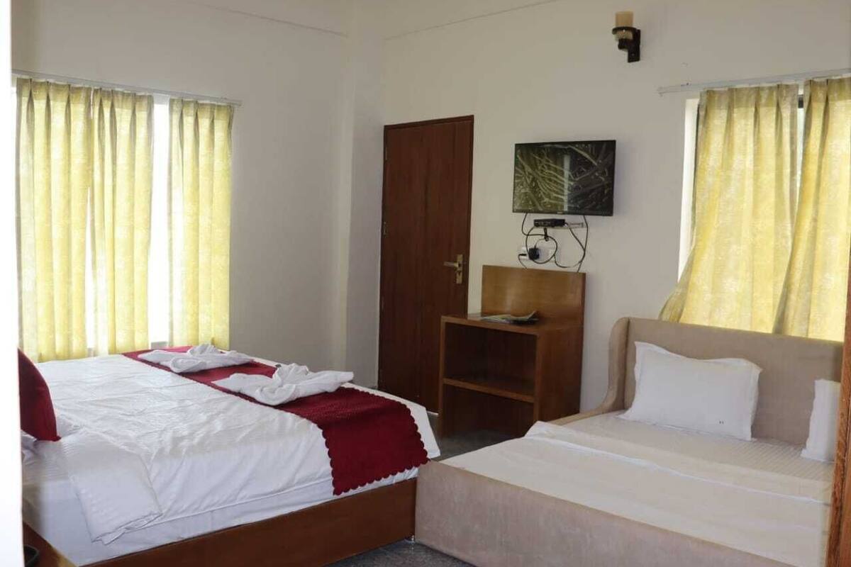 Une chambre d’hôtel avec deux lits, une armoire en bois, une petite table et un téléviseur fixé au mur.