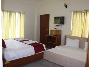 Ett hotellrum med två sängar, en garderob i trä, ett litet bord och en tv som är monterad på väggen.