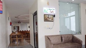Un espace d’accueil avec un canapé, un coin repas avec des tables et des chaises en bois, un panneau décoratif sur le thème de la nature et une porte en verre donnant sur une autre pièce.