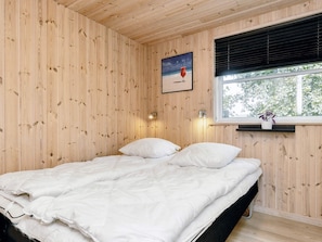 A wooden-paneled room with a bed, a window with a view, and a wall-mounted light fixture. - 5 Star Holiday Home in Idestrup (Idestrup)