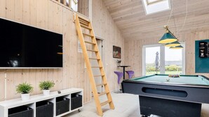 A room with a pool table, a TV mounted on a wooden wall, a wooden ladder, and a window with a view. - 5 Star Holiday Home in Idestrup (Idestrup)