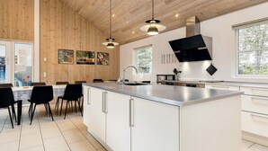 A modern kitchen with a central island, pendant lighting, and a view of the outdoors through large windows. - 5 Star Holiday Home in Idestrup (Idestrup)