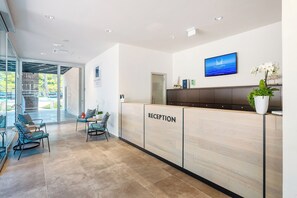 A reception area with a wooden reception desk, a flat-screen TV displaying 'Santa Marina', and a potted plant. - Premium Camping Homes Santa Marina (Tar-Vabriga)