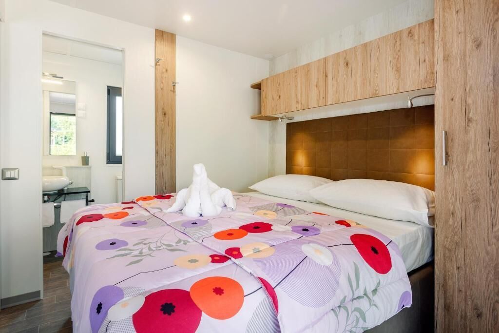 Ein Schlafzimmer mit einem hölzernen Kopfende, einem Bett mit floralem Überwurf und einem weißen Dekorationsgegenstand auf dem Bett.