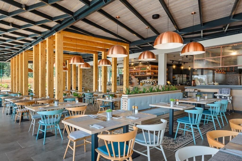 An indoor dining area with wooden beams, blue and white chairs, and copper pendant lights.